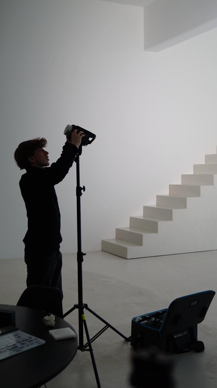 Behind-the-scenes Foto eines Fotografen im hellen Studio vor einer Treppe.